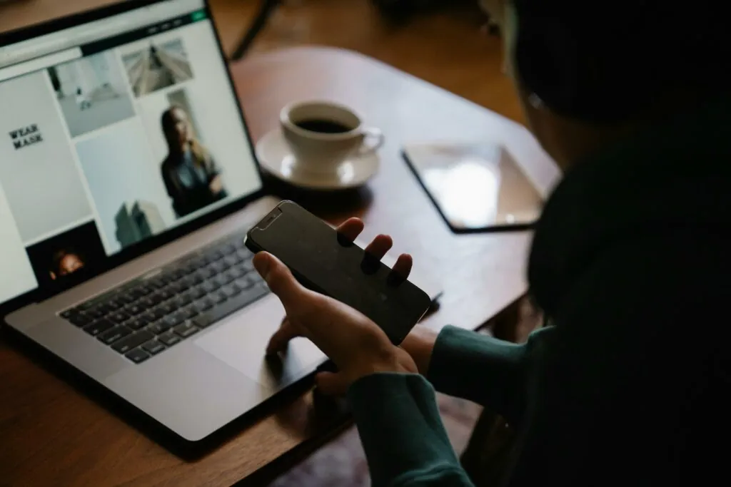 a person holding a phone and looking at a laptop screen